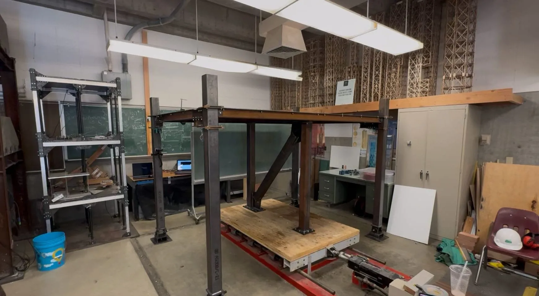 A steel model structure bolted to a shake table in a Cal Poly lab, with a CHIIP unit in each corner.